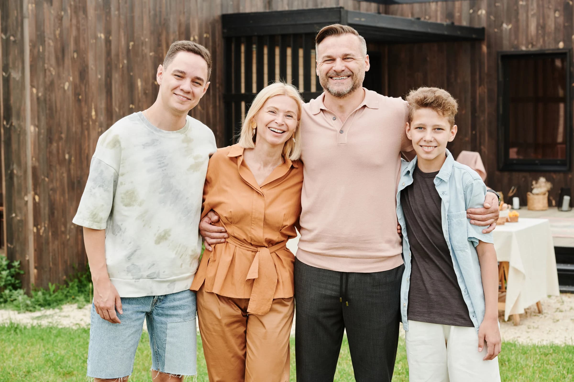 Family of four standing together outside a wood-sided home