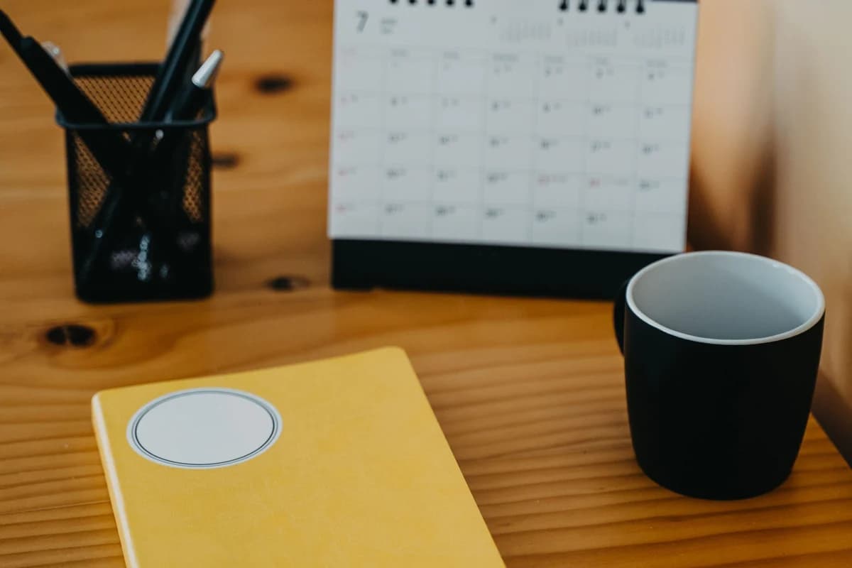 Desk calendar, notebook and mug on a warm wooden table